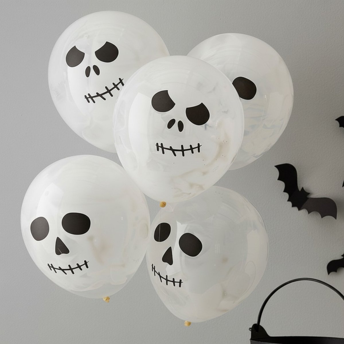 Hvide balloner med sorte skeletansigter, sat på et gråt bord med flere balloner i baggrunden