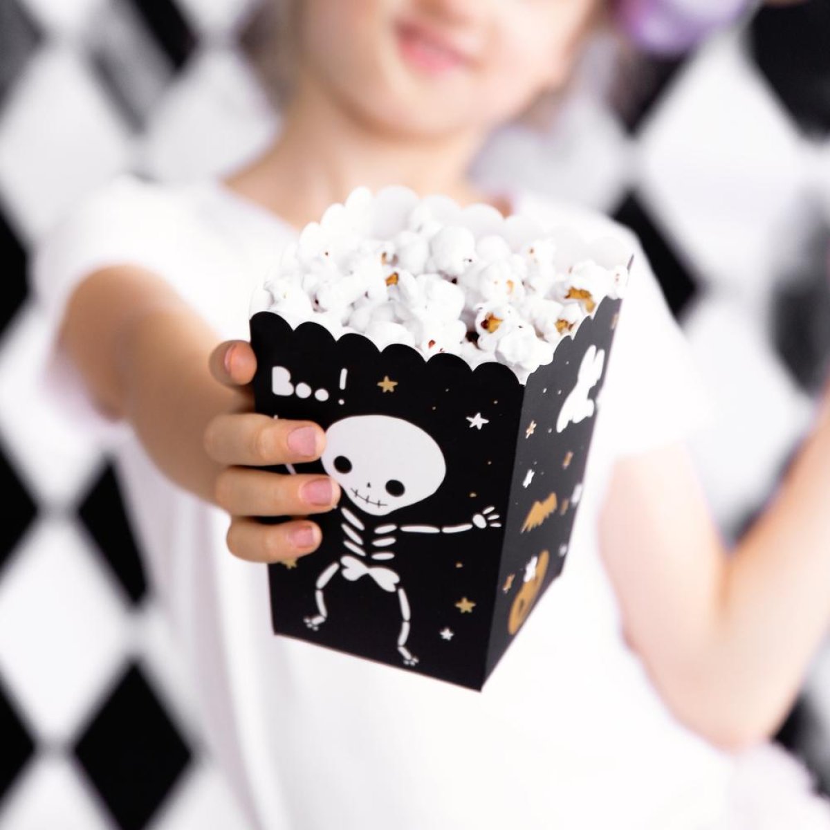 Sort popcornbæger med skelet-print, holdt af et barn