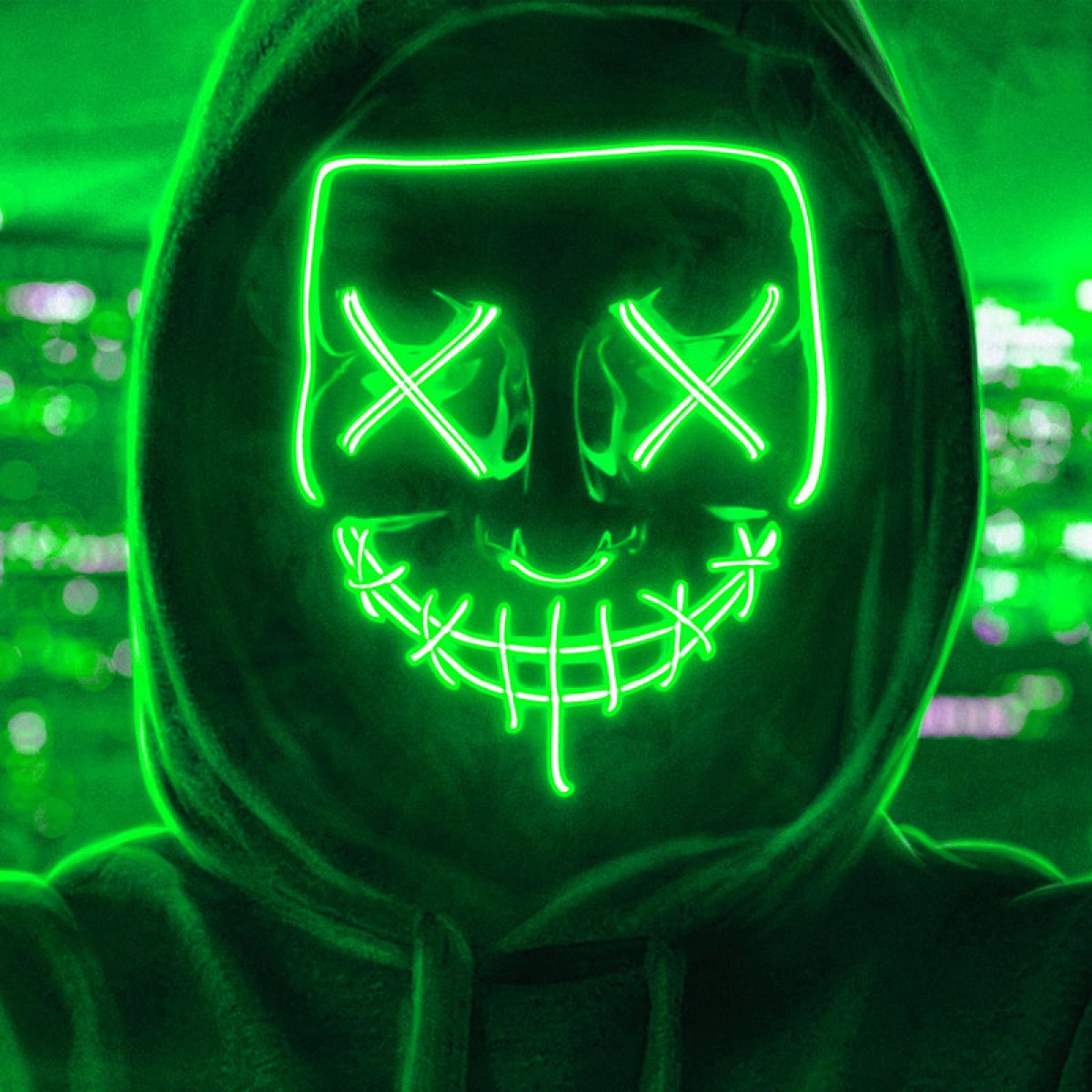 Person med sort hætte og grøn LED-maske med lysende øjne og mund, set mod et mørkt rum